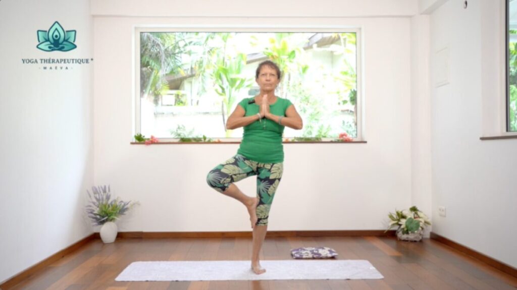 Posture de l'arbre : une femme debout mains jointes sur la poitrine avec une jambe pliée au niveau du genou opposé/