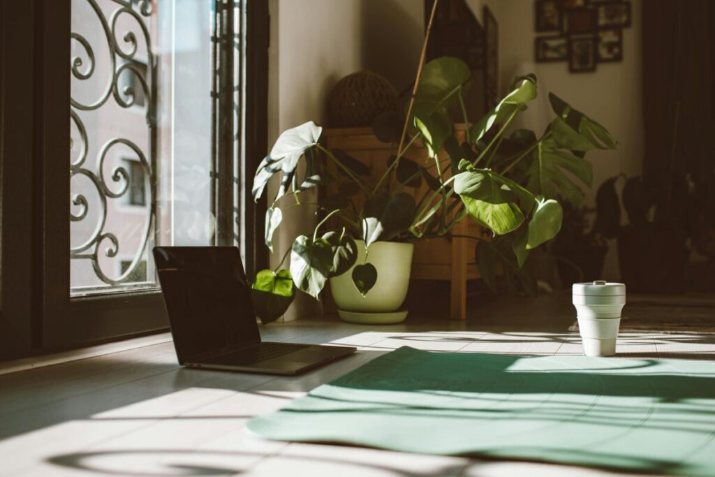 Un tapis de yoga avec un ordinateur, une plante et une tasse pour illustrer les cours de yoga en ligne.
