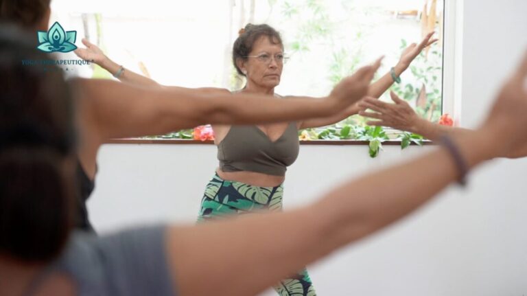 Une professeure donne des cours de yoga thérapeutique face à plusieurs personnes dont on ne voit que les bras.