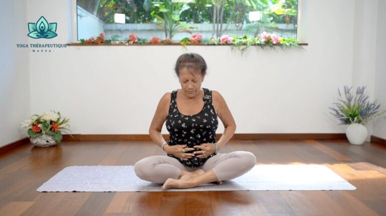 une femme assise en tailleur touche et regarde son ventre