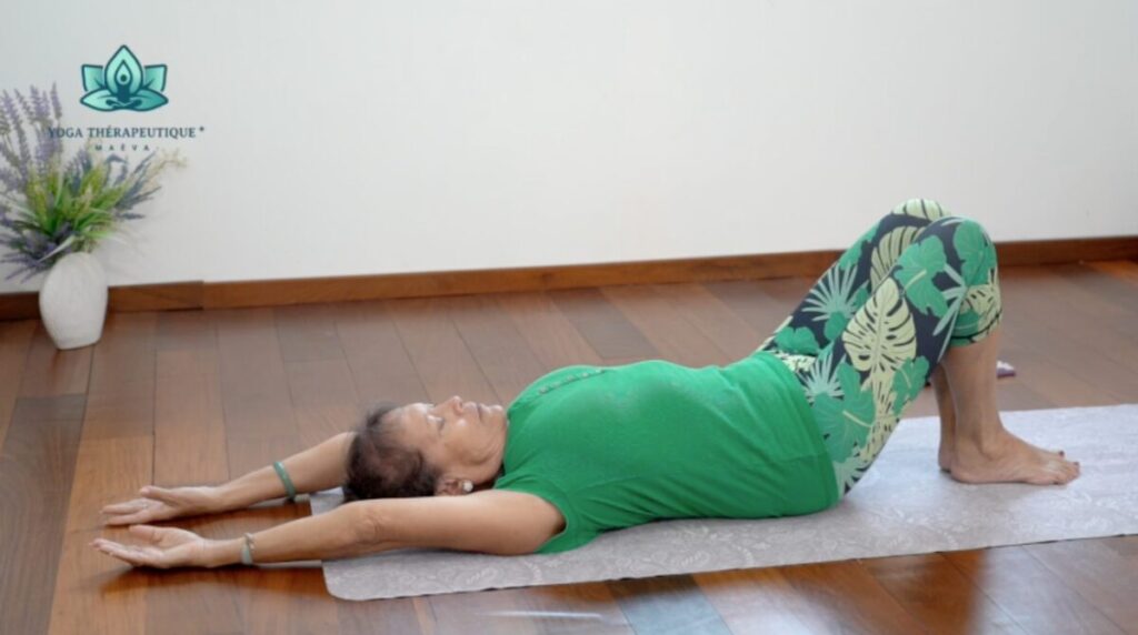 Une femme couchée sur le dos, les jambes pliées, les bras tendus derrière sa tête. Étirement du haut du corps.