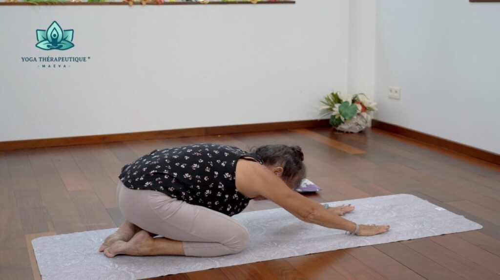 Posture de l'enfant : une femme assise sur ses pieds se penche en avant les bras au-dessus de sa tête